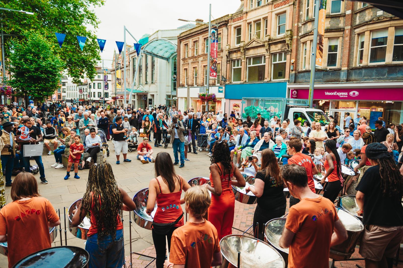 Large crowd of people in town centre watching steel pans